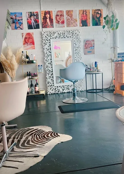 The studio's single salon chair on a zebra-print rug, facing an ornate white mirror and a wall of vintage hair posters