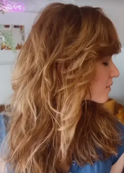 Side profile of a long, layered strawberry-blonde shag with a swept fringe